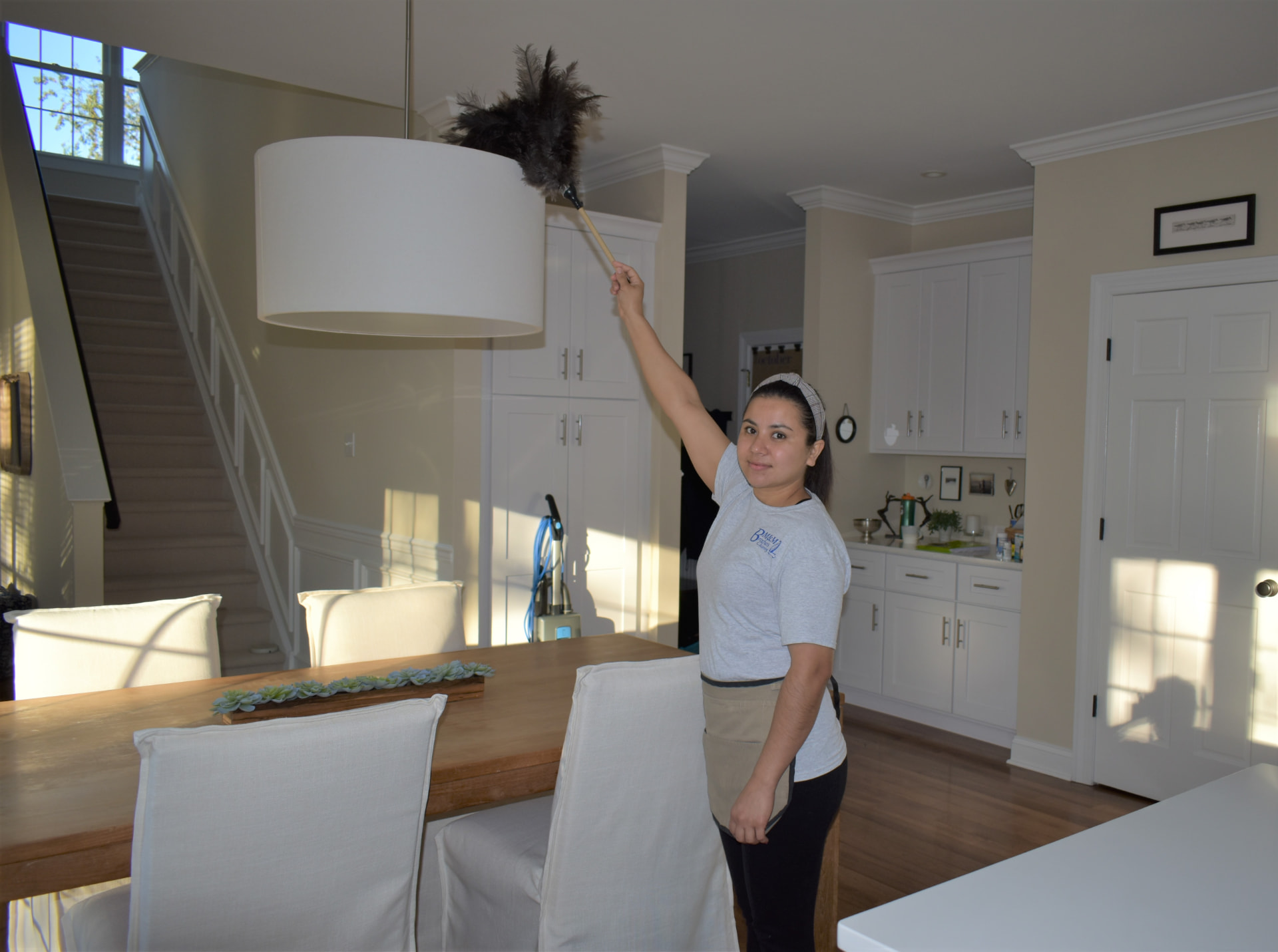 M & M Brothers team member dusting a light fixture in a bright dining room